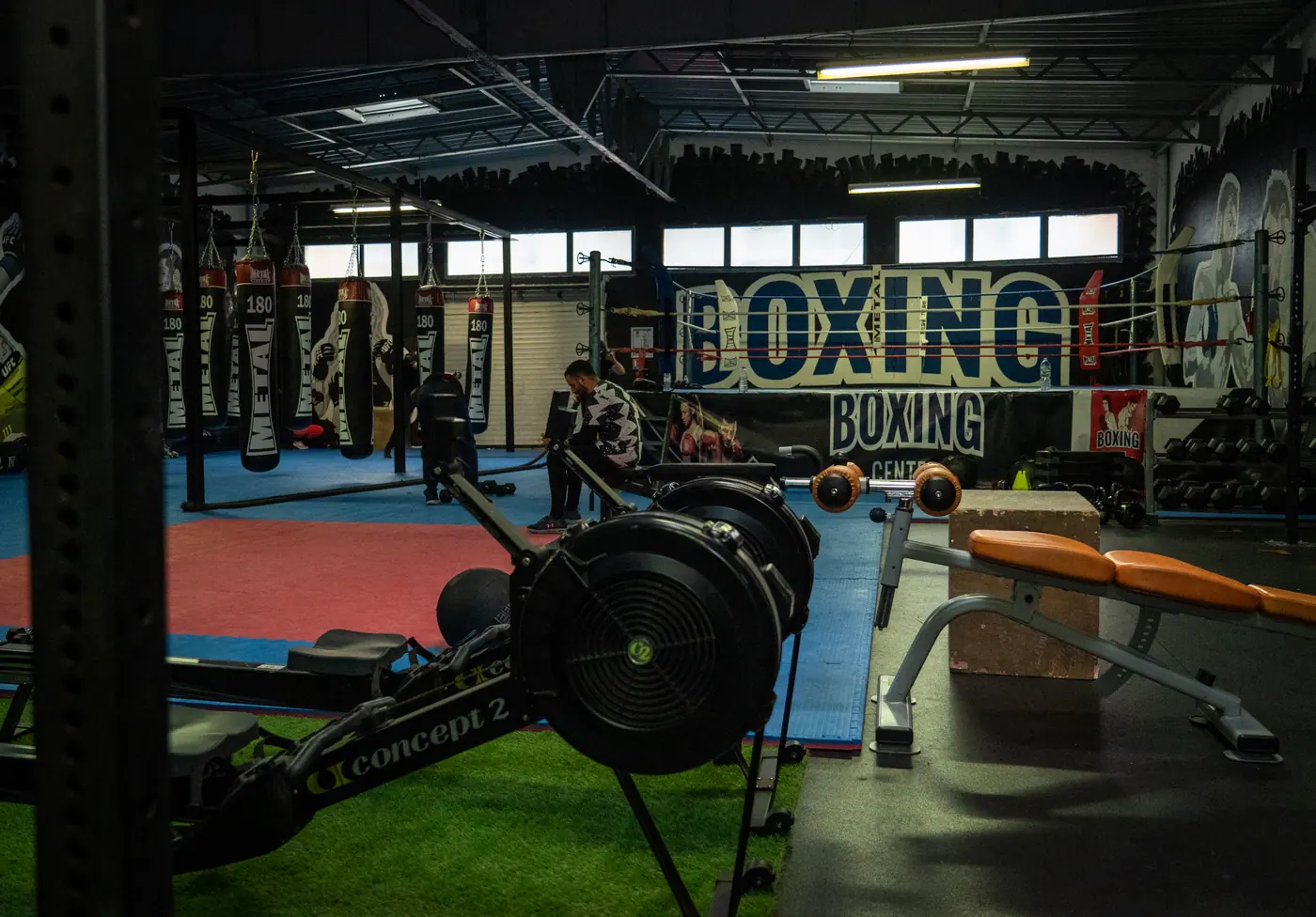 La zone moteur : rameurs alignés au premier plan, bancs et racks derrière, bannière Boxing Center au mur